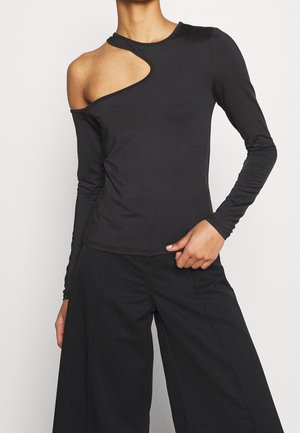 Haut noir à manches longues avec une découpe asymétrique à l'épaule, texture lisse et silhouette ajustée. Associe à un pantalon évasé.