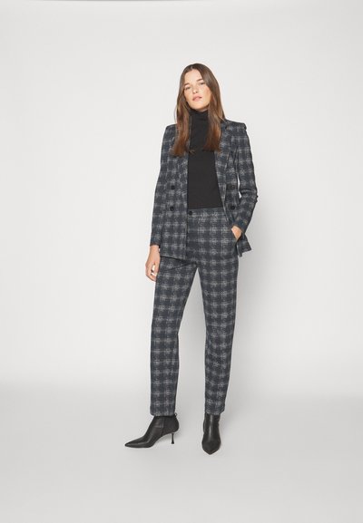 Skræddersyet ternet jakkesæt i navy og grå, der har en dobbeltbrystet blazer og bukser med lige ben. Sort turtleneck og spidse ankelstøvler.