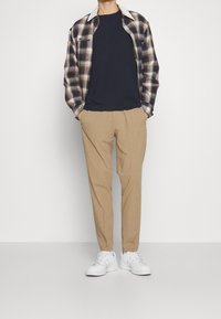Slidt ternet skjorte i marineblå, beige og hvid, parret med en marineblå T-shirt og beige bukser. Tilbehøret inkluderer hvide sneakers.