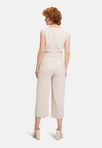Lys pink jumpsuit med fitted overdel, korte ærmer og brede bukser. Har en belagt talje og knaplukning bagpå. Glat tekstur.