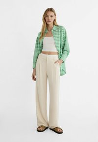 Zeleno-bíle pruhovaná košile na knoflíky přes bílé crop top, v kombinaci s béžovými širokými kalhotami a hnědými sandály.
