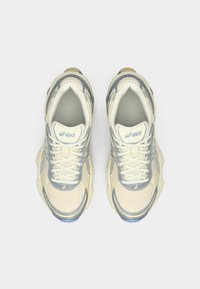 Fehér hálós sportcipők szürke és kék díszítéssel, kerek orral, strukturált talppal, és hangsúlyos fűzővel a biztos illeszkedés érdekében.