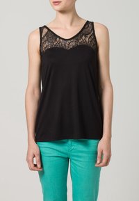 Top senza maniche nero con un pannello in pizzo sul colletto, caratterizzato da una superficie in tessuto liscia; abbinato a pantaloni turchesi brillanti.