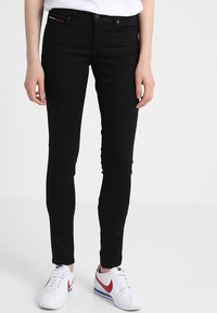 Vaqueros negros ajustados hechos de denim elástico, con una cintura de altura media, un diseño de cinco bolsillos y un sutile acento rojo en el bolsillo delantero.