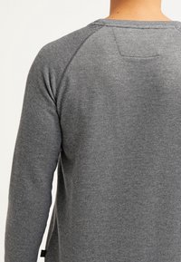 Felpa grigia a maniche lunghe con maglia testurizzata, maniche raglan e un piccolo dettaglio patch sul retro. Presenta una vestibilità comoda e un tessuto morbido.