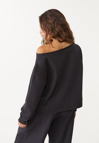 Czarna bluza z odkrytymi ramionami, wykonana z miękkiego materiału, z długimi rękawami i luźnym krojem, z prążkowanymi mankietami i ściągaczem.