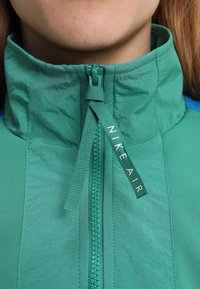 Nike Air-jacka med hög krage, tillverkad av texturerad grön tyg, med en hel dragkedja och en märkesdragrem.