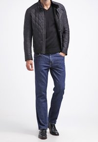 Czarna pikowana kurtka ze stójką, noszona na czarnym swetrze z dekoltem w serek, połączona z niebieskimi dżinsami i czarnymi skórzanymi butami.