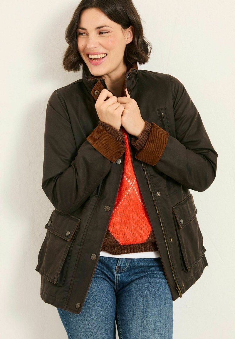 Brown waterproof jacket with corduroy accents, snap buttons, and multiple pockets, worn over an orange and brown patterned sweater.