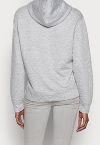 Grå vadderad hoodie med ett strukturerat mönster, designad med en huva och långa ärmar, i kombination med ljusgrå tajta byxor.