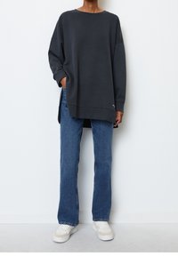 Sudadera extragrande de color gris oscuro con hombros caídos y aberturas laterales, combinada con jeans rectos azules y zapatillas blancas.