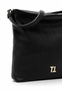 Schwarze Lederhandtasche mit glatter Textur, mit einem geschwungenen oberen Teil und einem kurzen Tragegurt. Goldene Beschläge zeigen auf einer Seite die Initialen "TL".