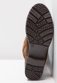 Botte en suede marron avec une semelle en caoutchouc noir texturé présentant un motif de crampons, taille 37 marquée sur le talon.