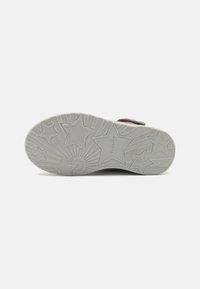 Suela de zapato de goma gris con un patrón de estrella y rayo de sol, que presenta el nombre de la marca y la talla en relieve. Diseño plano para estabilidad y tracción.