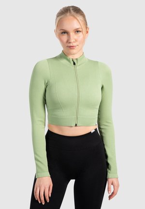 Lys grøn cropped zip-up jakke med ribbet tekstur, lange ærmer, høj krave og figursyet design, parret med højttaljede sorte leggings.