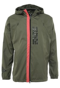 Chaqueta verde oliva con una franja vertical roja y un logo negro de tres rayas en la manga izquierda. Presenta una capucha y un cierre frontal con cremallera.