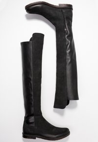 Botas negras de cuero y ante por encima de la rodilla. Presentan un zipper en el lateral, punta redondeada y un tacón bajo apilado con una textura suave.