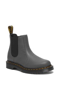 Botines de cuero gris hasta el tobillo con paneles laterales elásticos, suela de goma negra, costuras amarillas y una cinta de tirón amarilla en la parte posterior.