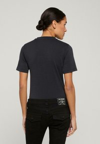 Czarny t-shirt z krótkim rękawem z okrągłym dekoltem, wykonany z miękkiej bawełny. Posiada prostokątną metkę marki na tylnym pasku ciemnych dżinsów.