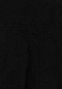 Tissu en lin noir avec une surface texturée, présentant une couture subtile et un petit détail de poche plate près du centre.