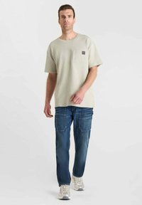 Lichtgrijs kortarmig shirt met een borstzak, gecombineerd met donkerblauwe cargo jeans met zichtbare stiksels en meerdere zakken.