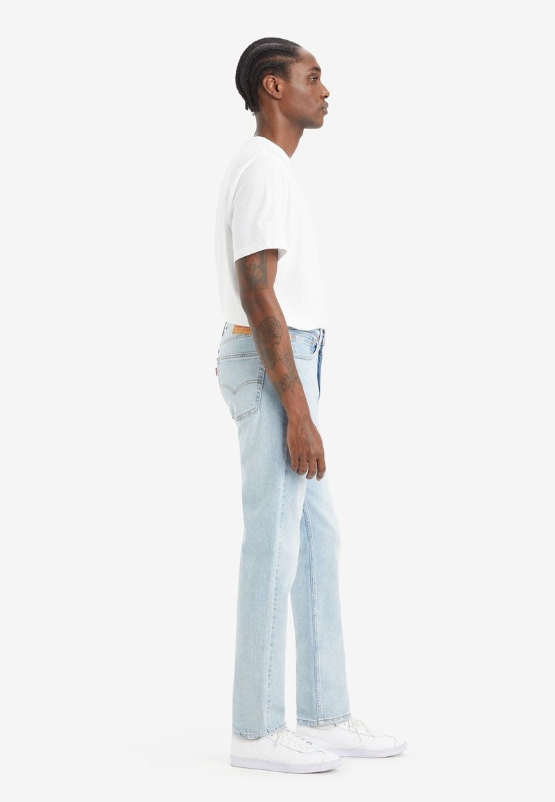 Lichtblauwe denim jeans met een rechte snit, gedragen met een eenvoudige witte t-shirt en witte sneakers. Beschikt over een leren achterpatch en gestikte accenten.