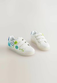 White children's sneakers with three Velcro straps, blue and green paint splatter designs, and round decorative patches on a light background.
