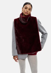 Burgundské umělé kožešinové nákrčník s širokým límcem, přes šedý blazer. Obsahuje hladkou texturu a obdélníkový tvar.