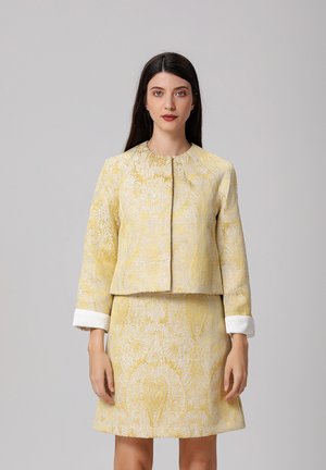 Ensemble de veste et jupe à motifs jaunes, avec de délicats motifs floraux blancs, un col rond et des accents de manche blancs. Texture de tissu lisse.