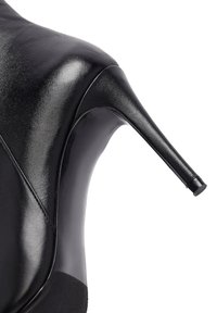 Chaussure à talons hauts noire en cuir brillant, avec un bout pointu et un talon stiletto fin et allongé. Texture lisse sans motifs visibles.