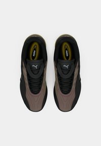 O pereche de adidași Puma negri și maro priviți de sus pe un fundal alb, arătând marca pe limbă și pe branturi.