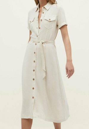 Beige midi skjortekjole med korte ærmer, knapper foran, to brystlommer med knapper og et stofbælte bundet i taljen.
