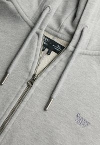 Felpa grigia con zip, caratterizzata da una texture a coste, coulisse e un logo ricamato sul lato sinistro del petto. Zip argentata con dettagli di branding.