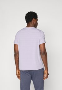 Camiseta de manga corta de color morado claro con escote redondo y sutiles rayas horizontales; hecha de una tela con textura suave.