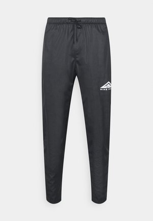 Pantalon de sport noir avec taille élastique et cordon, jambes fuselées, et un petit logo blanc Nike Trail sur la partie supérieure de la cuisse gauche.