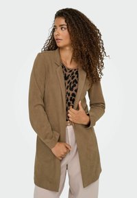Blazer de ante marrón con un diseño a medida, que presenta un cuello con muesca y mangas largas, combinado con una blusa de estampado de leopardo.