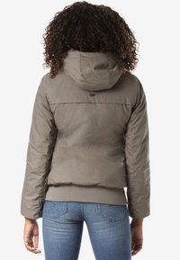 Khaki puchowa kurtka z kapturem, o gładkiej fakturze, z elastycznymi mankietami i obniżonym dołem, noszona na niebieskich dżinsach.