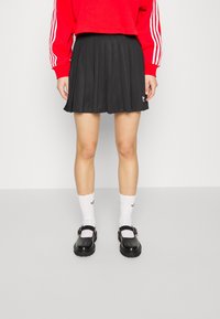 Czarna plisowana spódnica, zestawiona z białymi skarpetkami z falbankami i czarnymi butami Mary Jane. Strój składa się z czerwonego swetra z trzema białymi paskami.