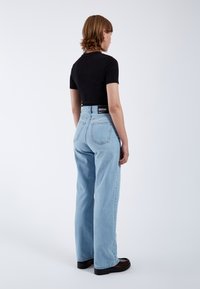 Jeans anchos de mezclilla azul claro con una cintura alta y dos bolsillos traseros; combinados con una blusa ajustada de manga corta negra. Textura suave.