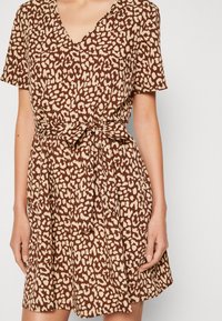 Hnědé šaty s leopardím potiskem, krátké rukávy, výstřih do V a pásek v pase. Lehce látka s jemnou strukturou a rozšířenou sukňou.