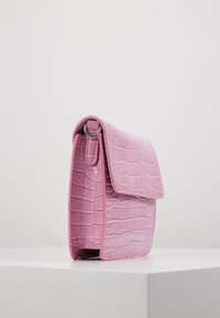 Borsa a tracolla in pelle embossata color rosa con chiusura a pattina, caratterizzata da un dettaglio hardware rotondo e una superficie liscia e lucida.