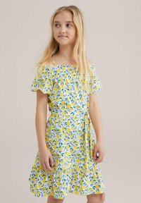 Gul blommig klänning med axelbandslösa ärmar, blå bladmönster och en volangkjol. Gjord av lätt tyg; inkluderar en knytning i midjan.