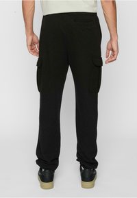 Black cargo pants with a relaxed fit, featuring side pockets and a back pocket, made from soft fabric, with a smooth texture and elastic waistband.