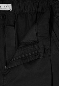 Pantaloni neri con vita elastica, chiusura con zip e tasche laterali. Il materiale sembra liscio con una finitura opaca e dettagli di cuciture minimi.