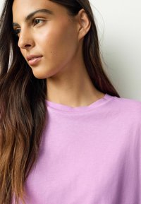 Hellviolettes Baumwoll-T-Shirt mit Rundhalsausschnitt und kurzen Ärmeln, das eine weiche Textur und ein einfaches, klares Design aufweist.