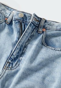 Vaalean siniset farkut, joissa on vetoketjuflappi, metalliknapin kiinnitys ja kuparin niittejä. Ne ovat pehmeät ja niissä on lievästi kuluneita merkkejä.