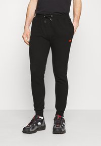 Svarta sweatpants i mjukt tyg, med en dragsko i midjan och en broderad flerfärgad logotyp på sidan. Fitted mudd vid anklarna.