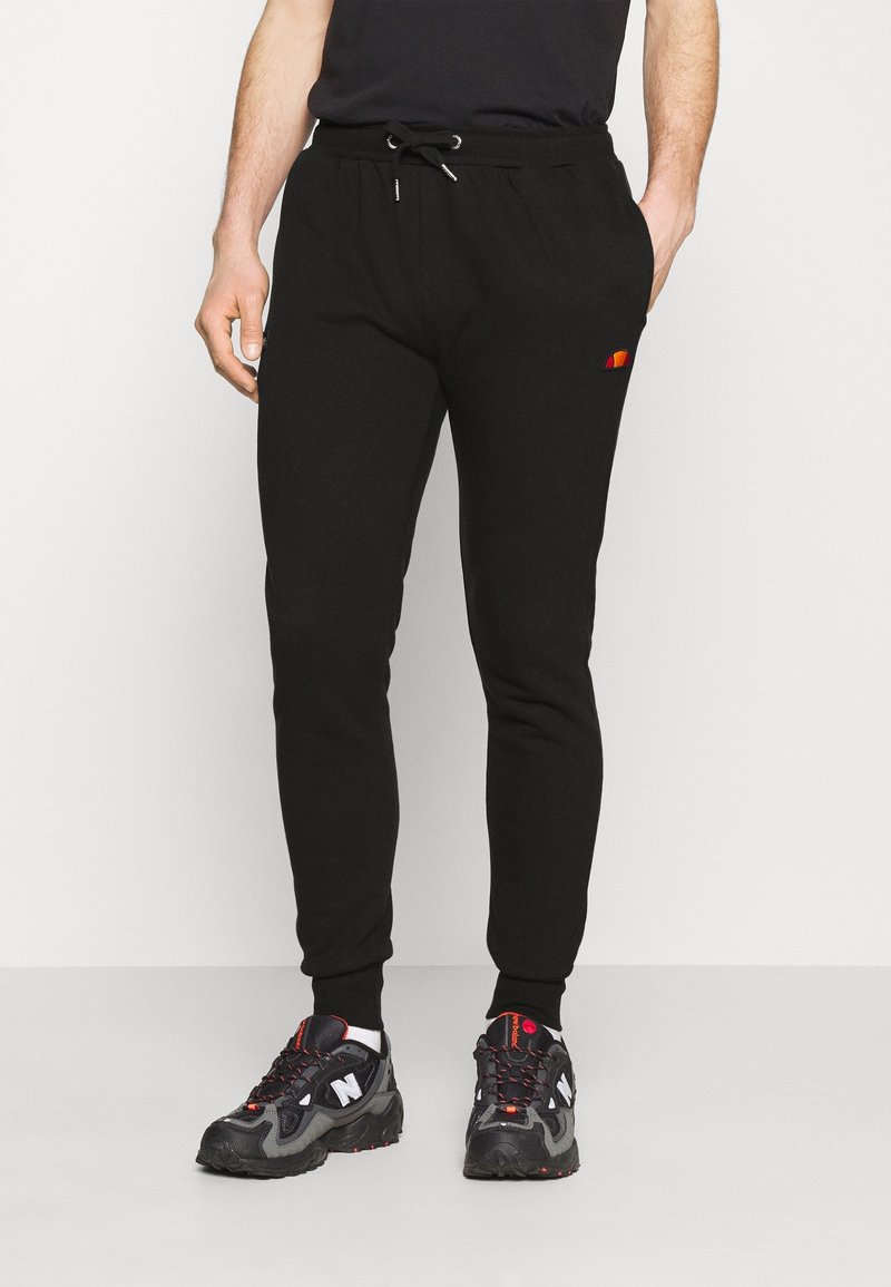 Svarta sweatpants i mjukt tyg, med en dragsko i midjan och en broderad flerfärgad logotyp på sidan. Fitted mudd vid anklarna.