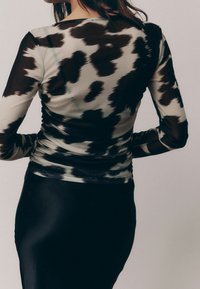 Black and cream sheer long-sleeve top featuring a cow print pattern, cinched waist, and soft texture, paired with a black skirt.