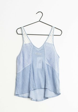 Světlomodrý proužkovaný tílko s výstřihem do V, krajkovými doplňky na ramenou a zakřiveným spodním lemem. Visí na černém kovovém háčku.